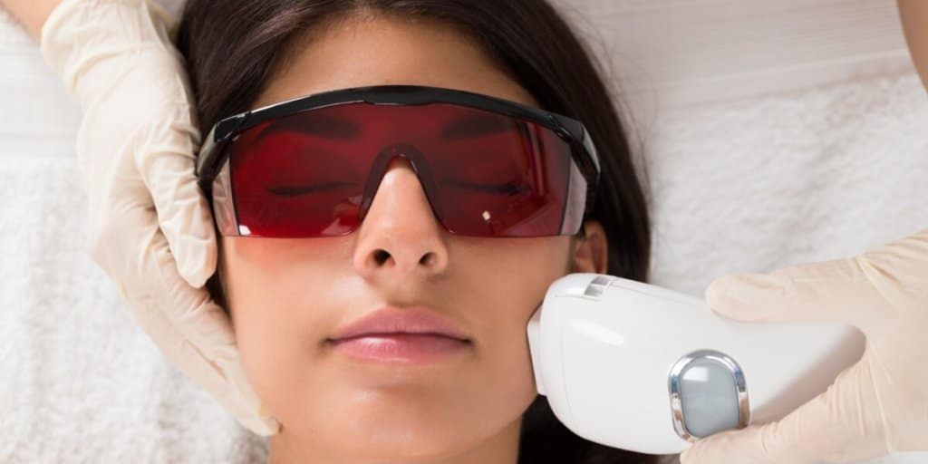 Eine Person mit Schutzbrille erhält eine Gesichtsbehandlung mit einem Lasergerät.